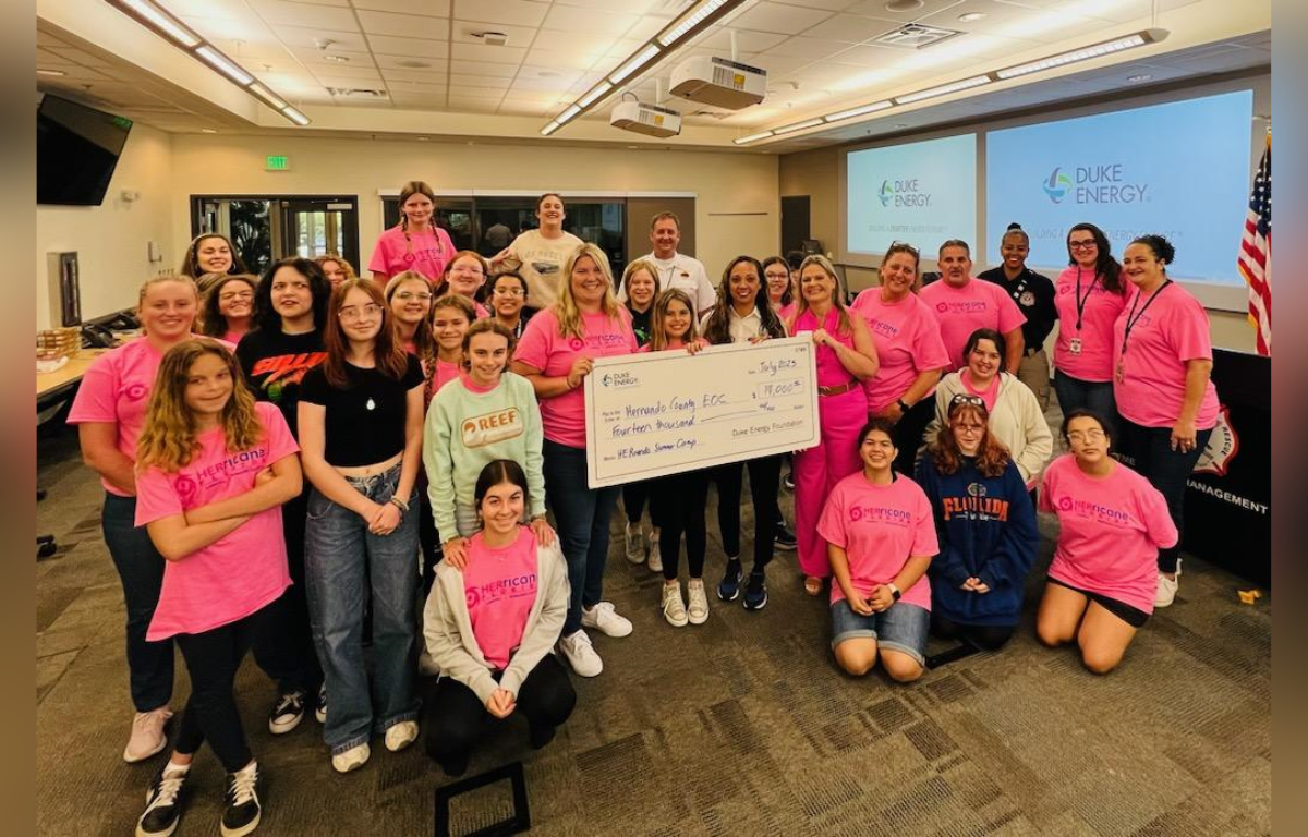 Students at HERricane Summer Camp posing with large check