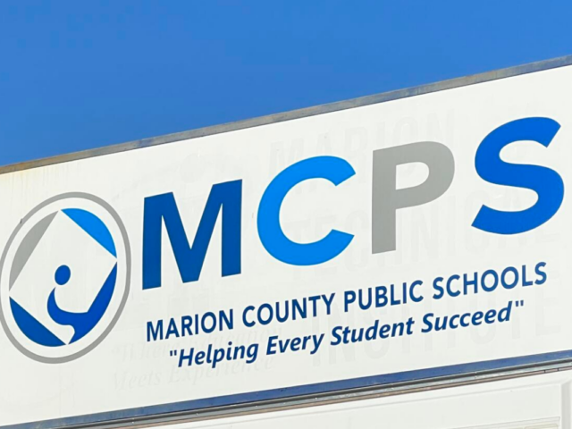 Marion County Public Schools sign displaying logo and motto, "Helping Every Student Succeed," against a clear blue sky.