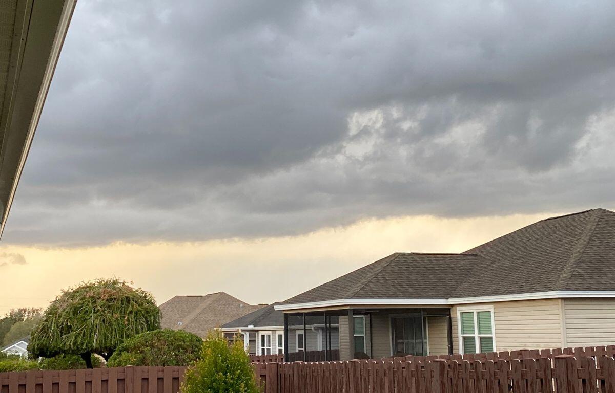 Dark storm clouds gather over rooftops and a wooden fence in a residential neighborhood.