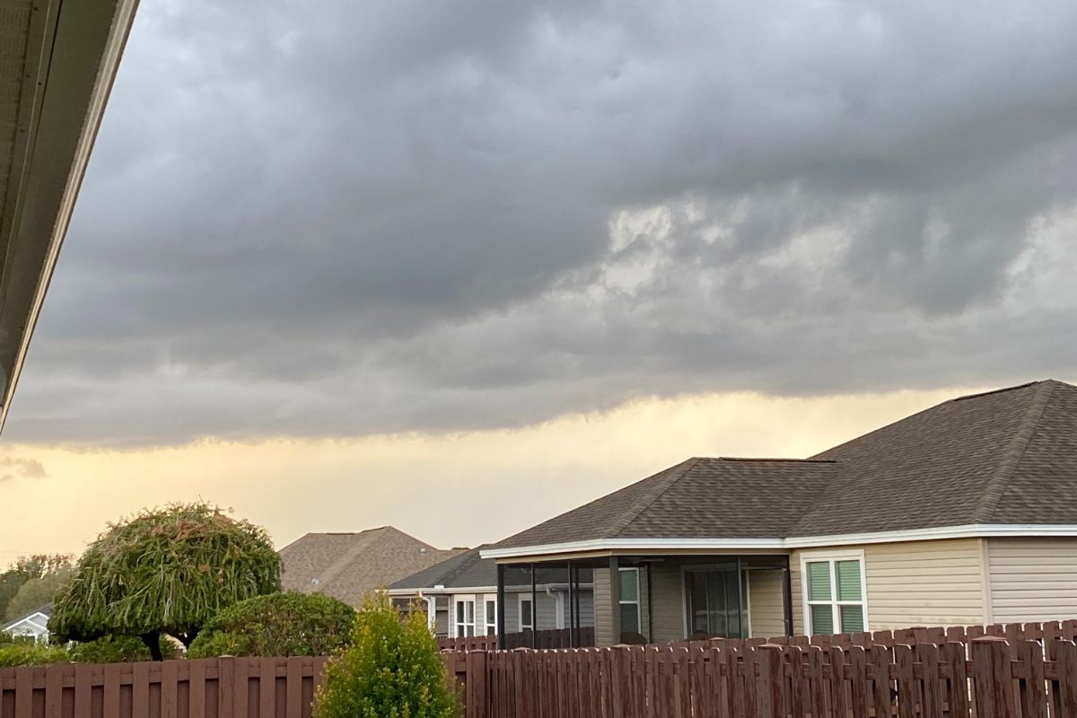 Dark storm clouds gather over rooftops and a wooden fence in a residential neighborhood.