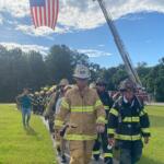 First responders in uniform walk beneath a raised American flag during a PTSD Awareness event at a park in Ocala.