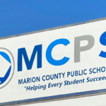 Marion County Public Schools sign with slogan "Helping Every Student Succeed" against a blue sky.