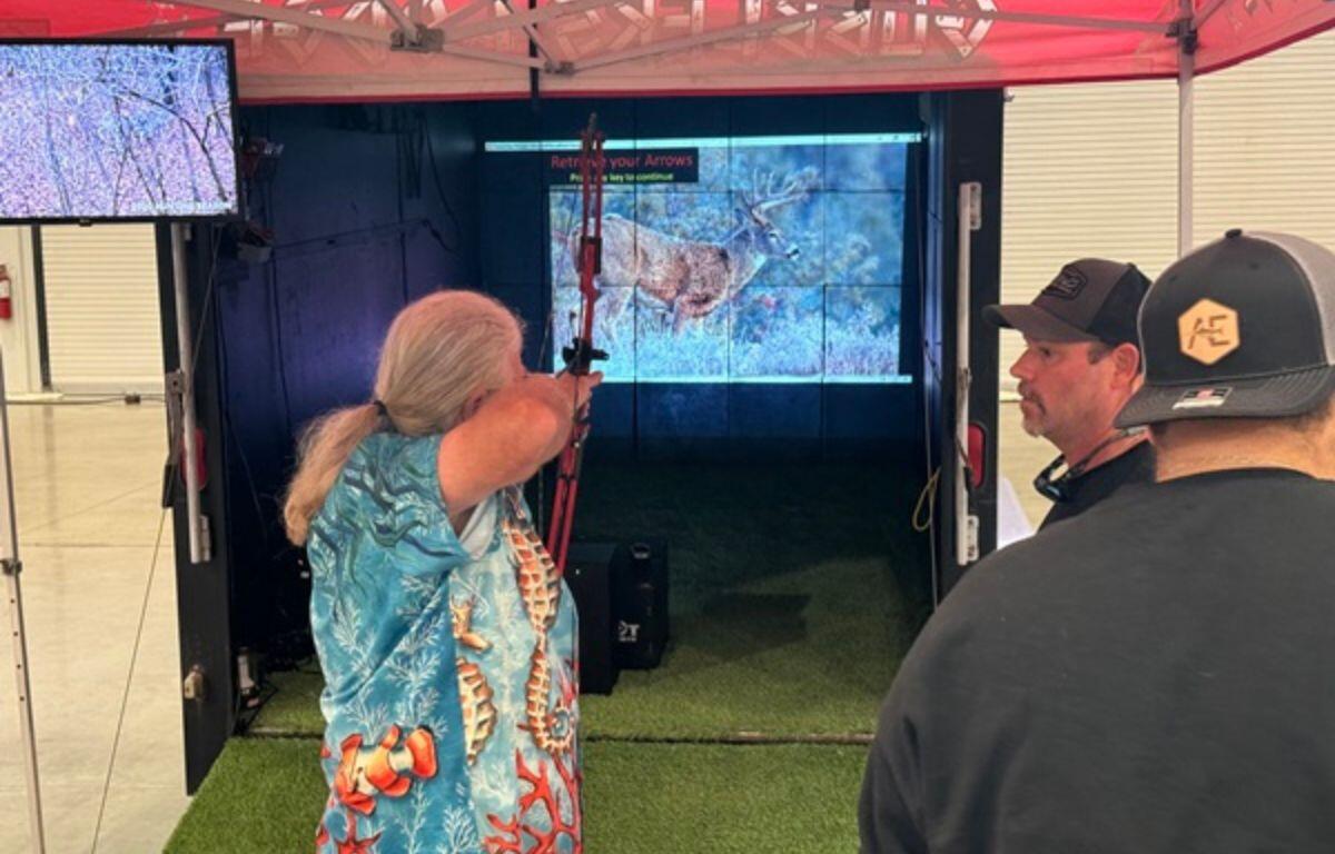 Woman aiming a bow at a virtual archery target at the North Central Florida Outdoor Expo.