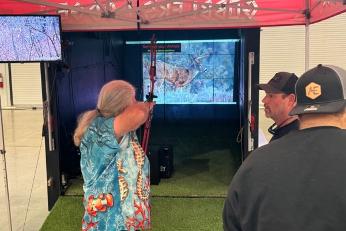Woman aiming a bow at a virtual archery target at the North Central Florida Outdoor Expo.