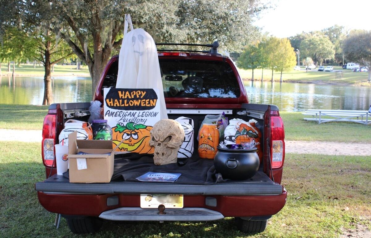 A decorated truck bed featuring Halloween props, including a skull, plastic pumpkins, and a “Happy Halloween” sign from the American Legion Auxiliary, set up beside a lake.