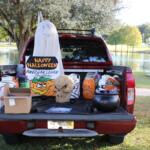 A decorated truck bed featuring Halloween props, including a skull, plastic pumpkins, and a “Happy Halloween” sign from the American Legion Auxiliary, set up beside a lake.