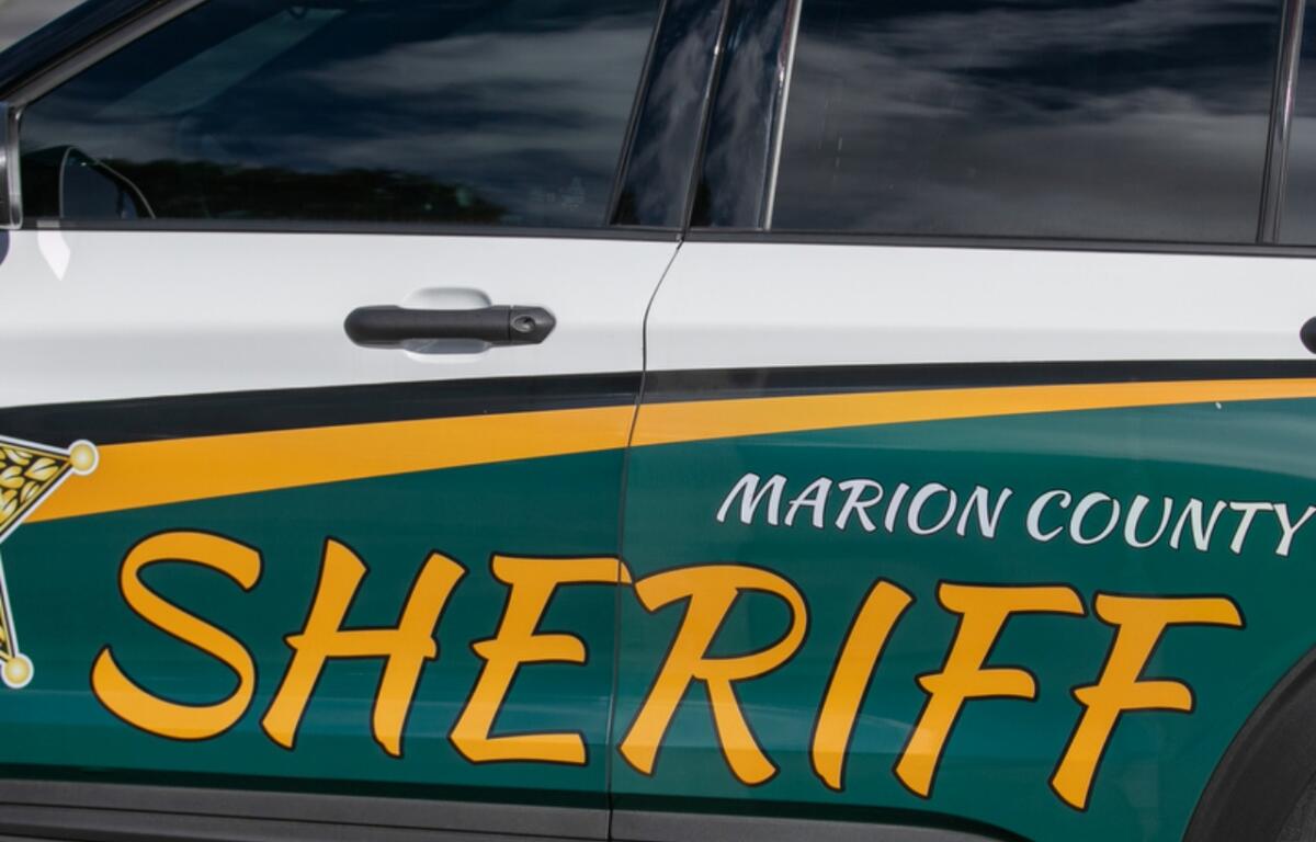 Green and white law enforcement vehicle with lettering on the front, and a street scene in the background.