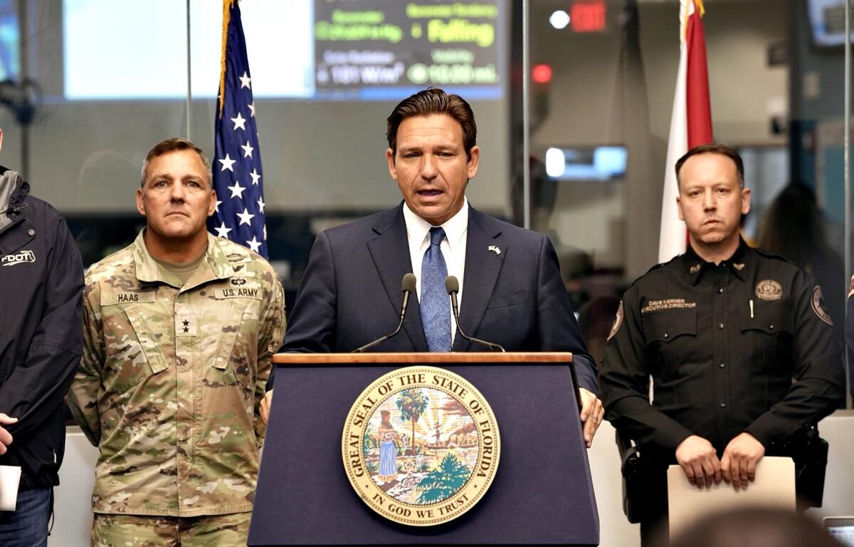 Florida Gov. Ron DeSantis speaks at a podium flanked by law enforcement and military officials during a press conference.