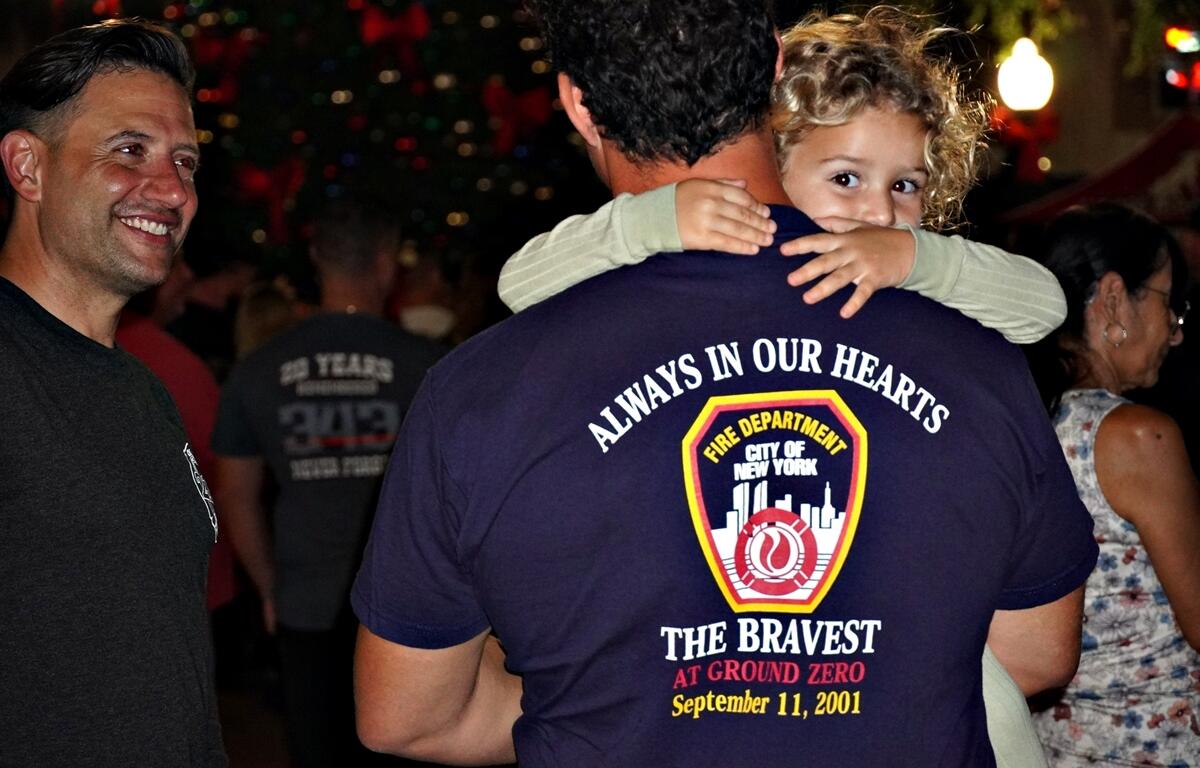 Little girl looking over man's shoulder. Back of shirt honors FDNY at 9-11.