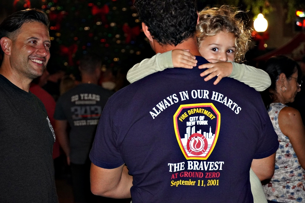 Little girl looking over man's shoulder. Back of shirt honors FDNY at 9-11.