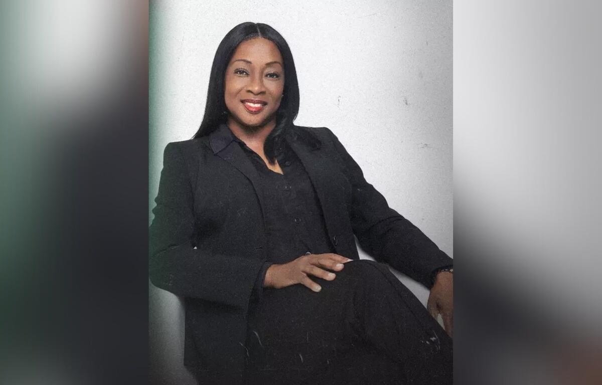 Angela Suggs, seated and smiling in a black suit against a light background.