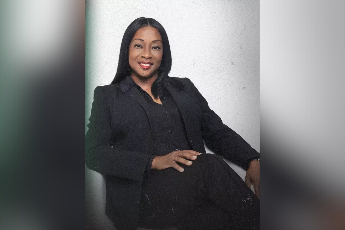 Angela Suggs, seated and smiling in a black suit against a light background.