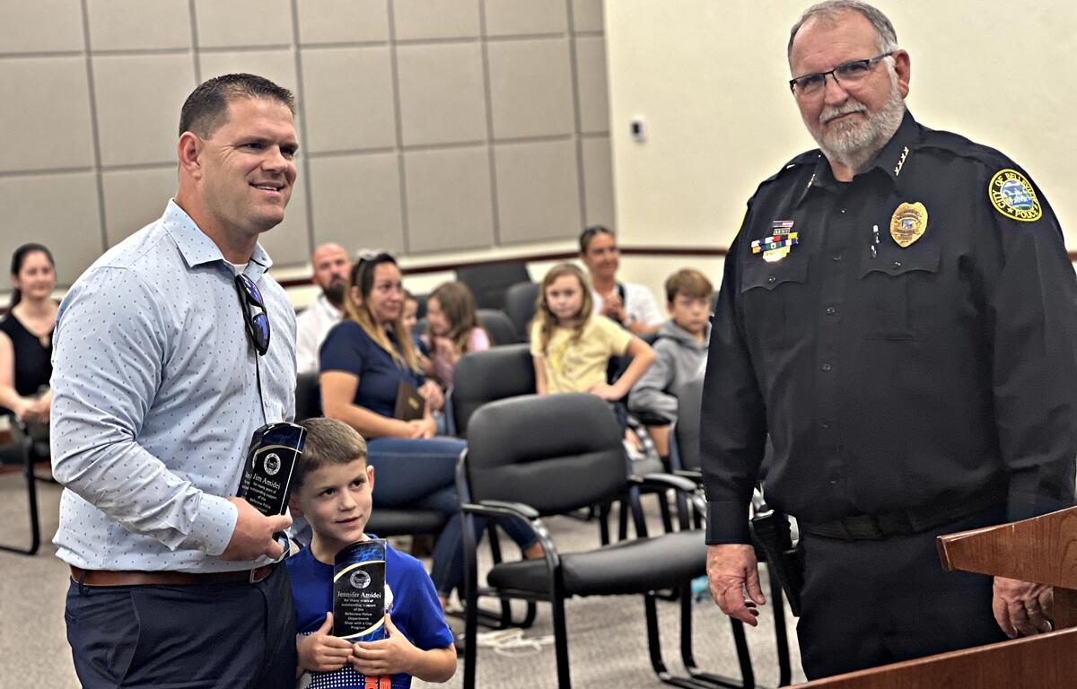Jennifer and Jim Amidei receive the Award of Gratitude from Belleview Police Chief Terry Holland during the Belleview City Commission meeting on Feb. 4, 2025. The couple was recognized for their dedication to the "Shop with a Cop" program, which provides holiday shopping trips for children in need.