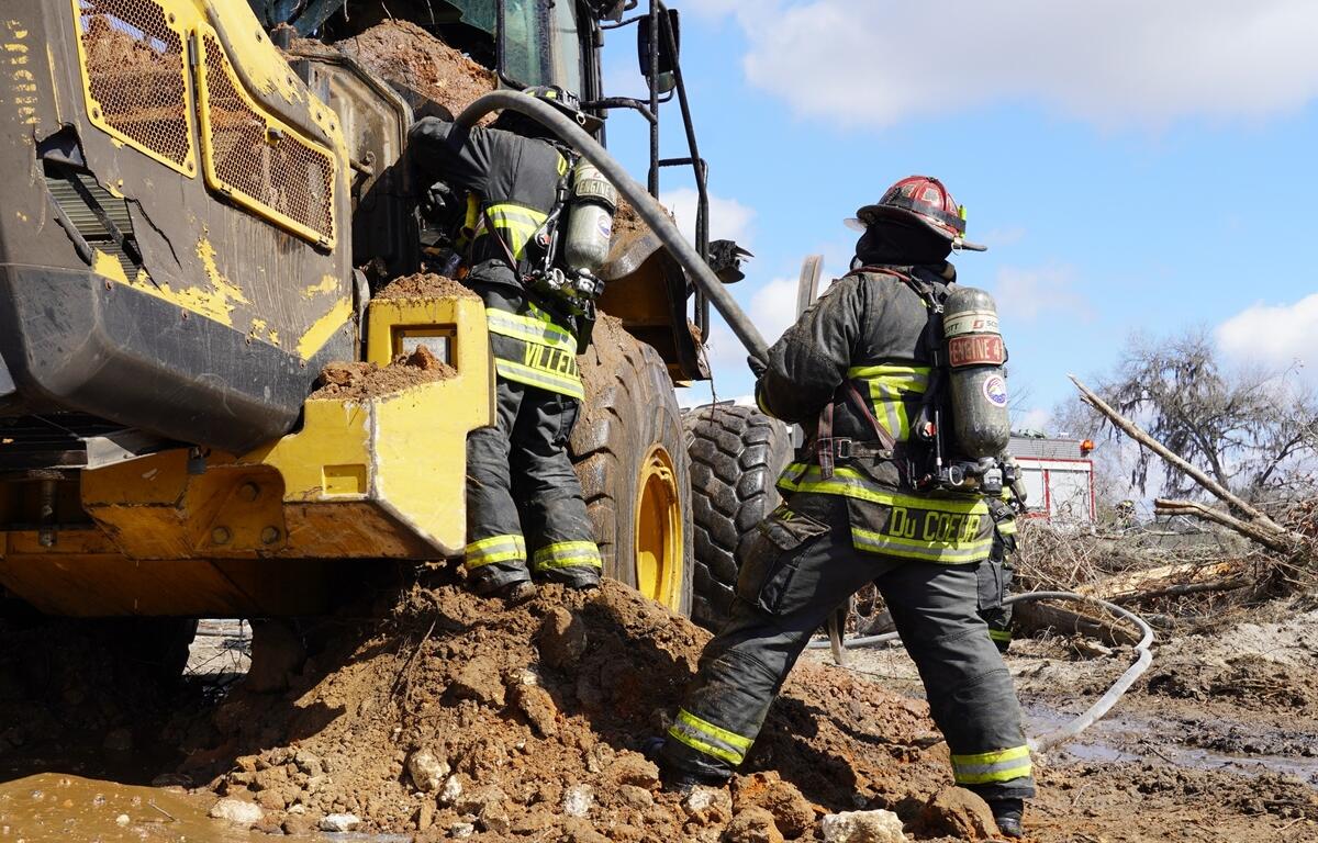 Ocala Fire Rescue firefighters work to extinguish a front-end loader fire on NW 11th Street, preventing the flames from spreading to nearby vegetation and containing a diesel spill.