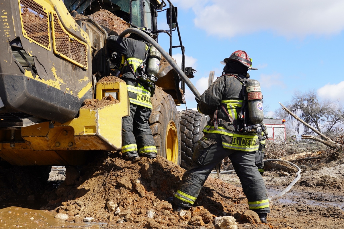 Ocala Fire Rescue firefighters work to extinguish a front-end loader fire on NW 11th Street, preventing the flames from spreading to nearby vegetation and containing a diesel spill.