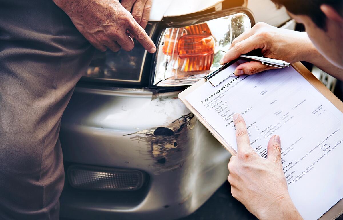 An insurance adjuster reviews a personal accident claim form next to a damaged vehicle following a collision. In Florida, drivers must carry Personal Injury Protection (PIP) and Property Damage Liability (PDL) coverage under the state’s no-fault insurance laws.