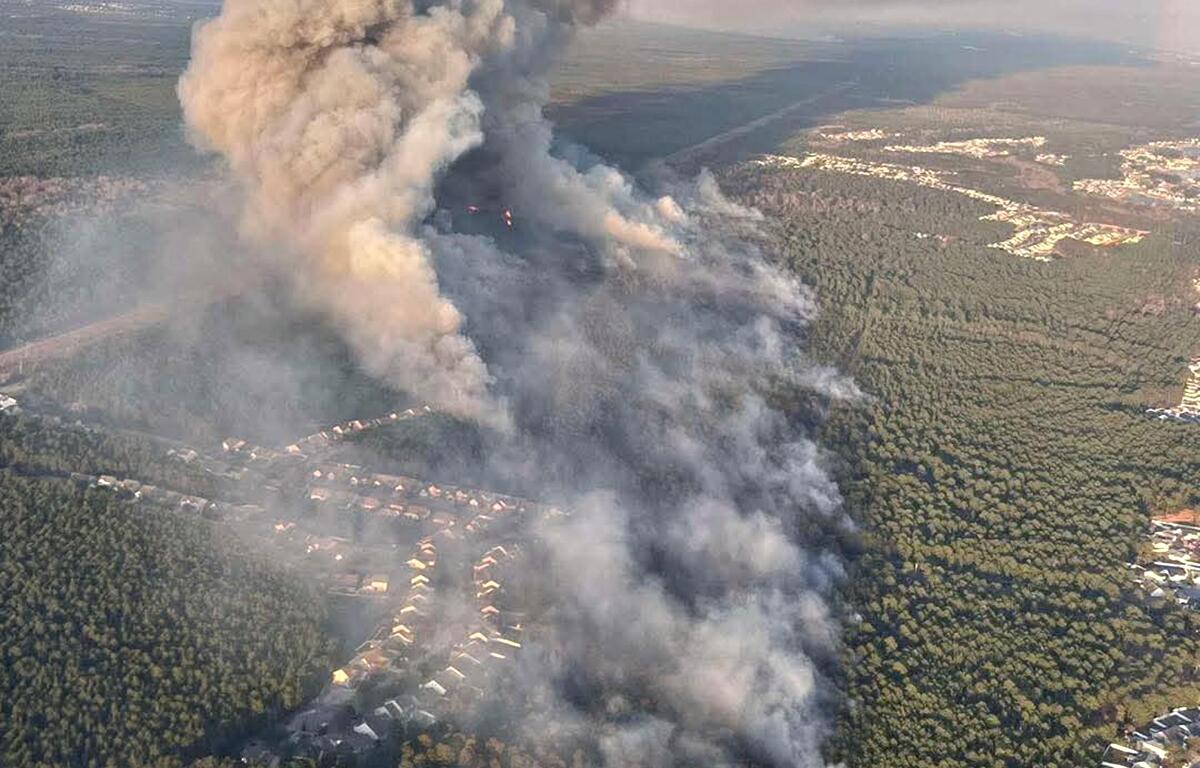 Flames and thick smoke rise as a wildfire burns through dry vegetation, threatening nearby homes and natural resources. Fire crews are working to contain the blaze as high winds and dry conditions fuel its spread.