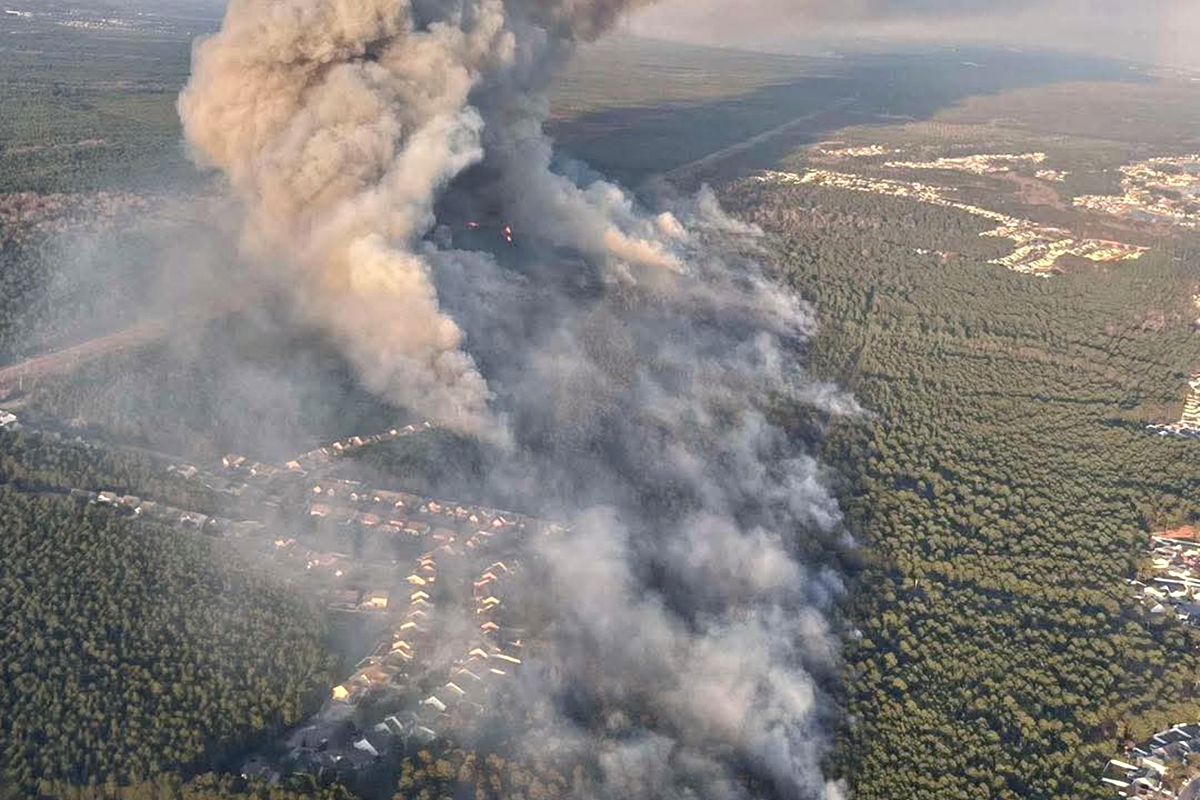 Flames and thick smoke rise as a wildfire burns through dry vegetation, threatening nearby homes and natural resources. Fire crews are working to contain the blaze as high winds and dry conditions fuel its spread.