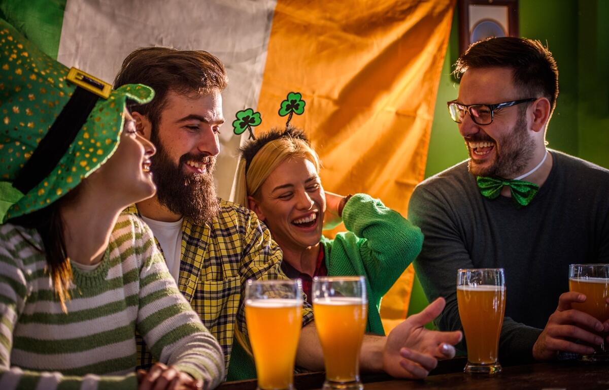 Friends celebrate St. Patrick's Day with drinks and laughter at a festive pub, dressed in green and Irish-themed accessories.