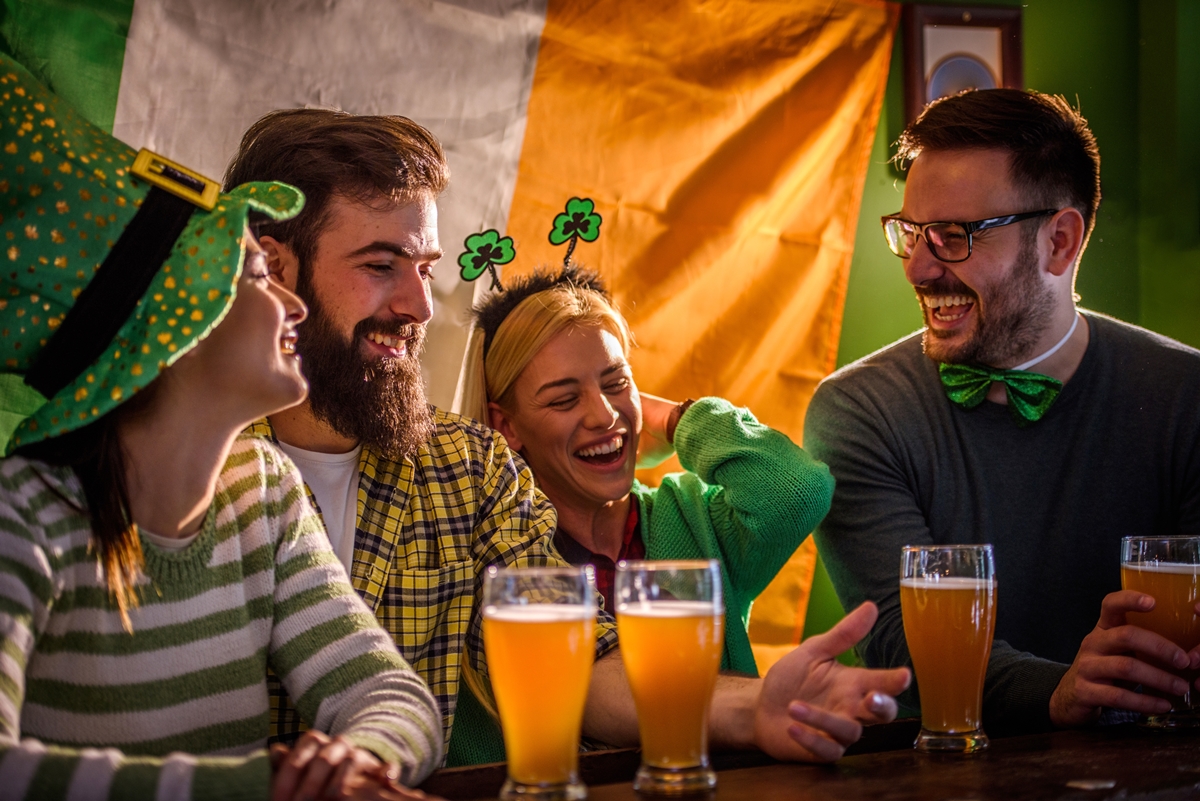 Friends celebrate St. Patrick's Day with drinks and laughter at a festive pub, dressed in green and Irish-themed accessories.