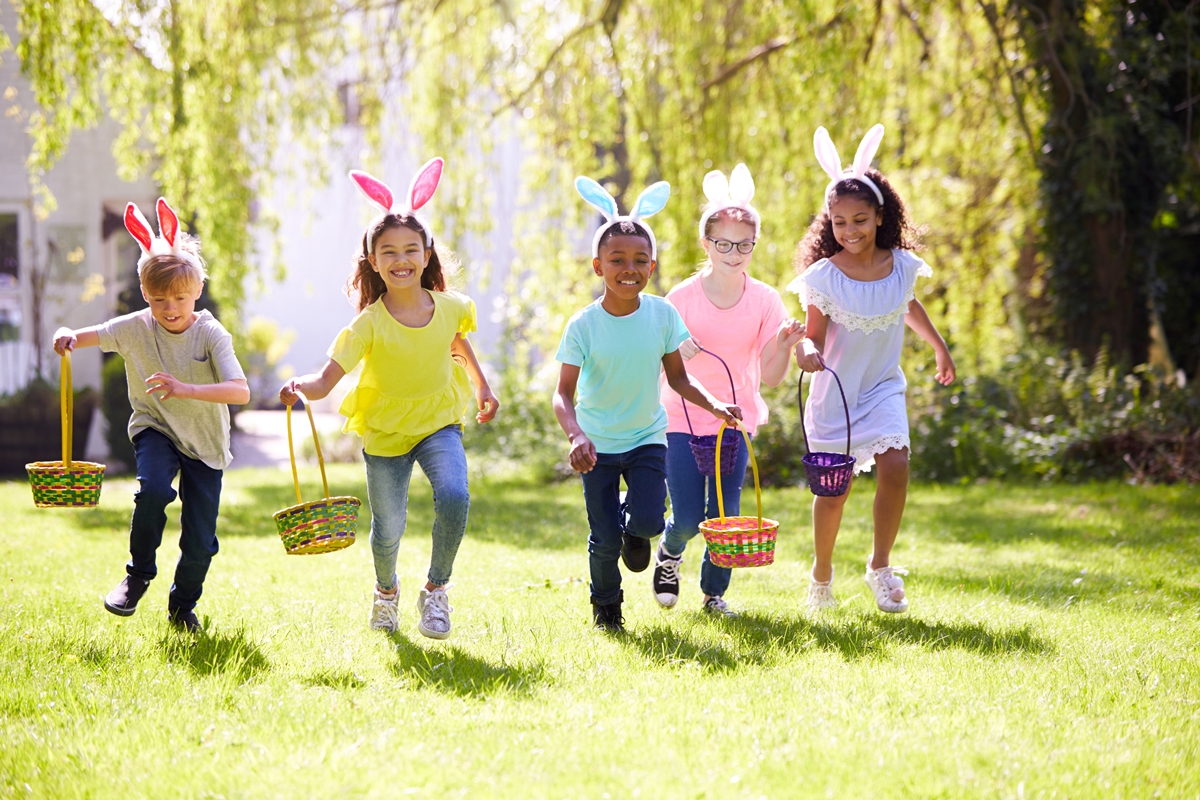 Children wearing bunny ears race through the grass with Easter baskets during a sunny spring egg hunt.