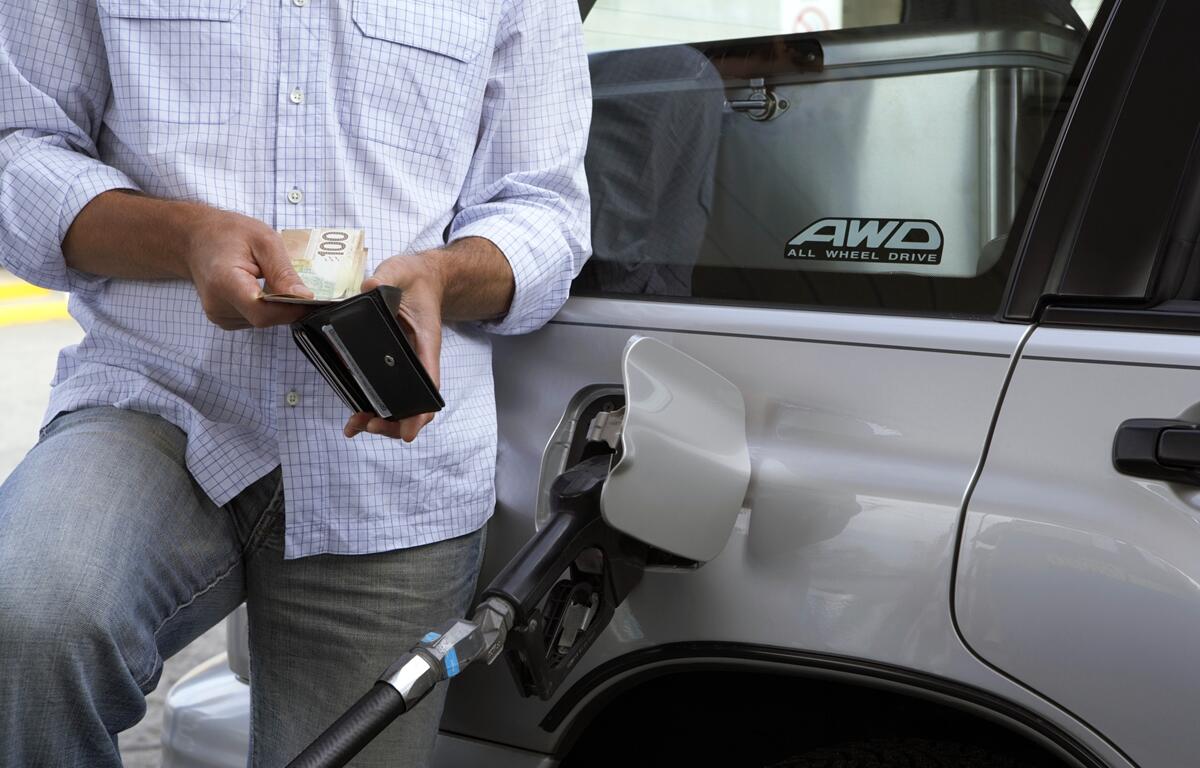 Person holding wallet and cash while fueling a vehicle at a gas station.