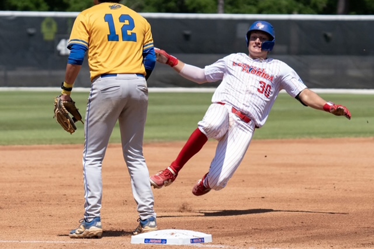 A College of Central Florida baseball player wearing a white pinstripe uniform and blue helmet slides into second base as a Gulf Coast State player in a yellow jersey stands nearby, glove in hand, during a Region 8 tournament game.