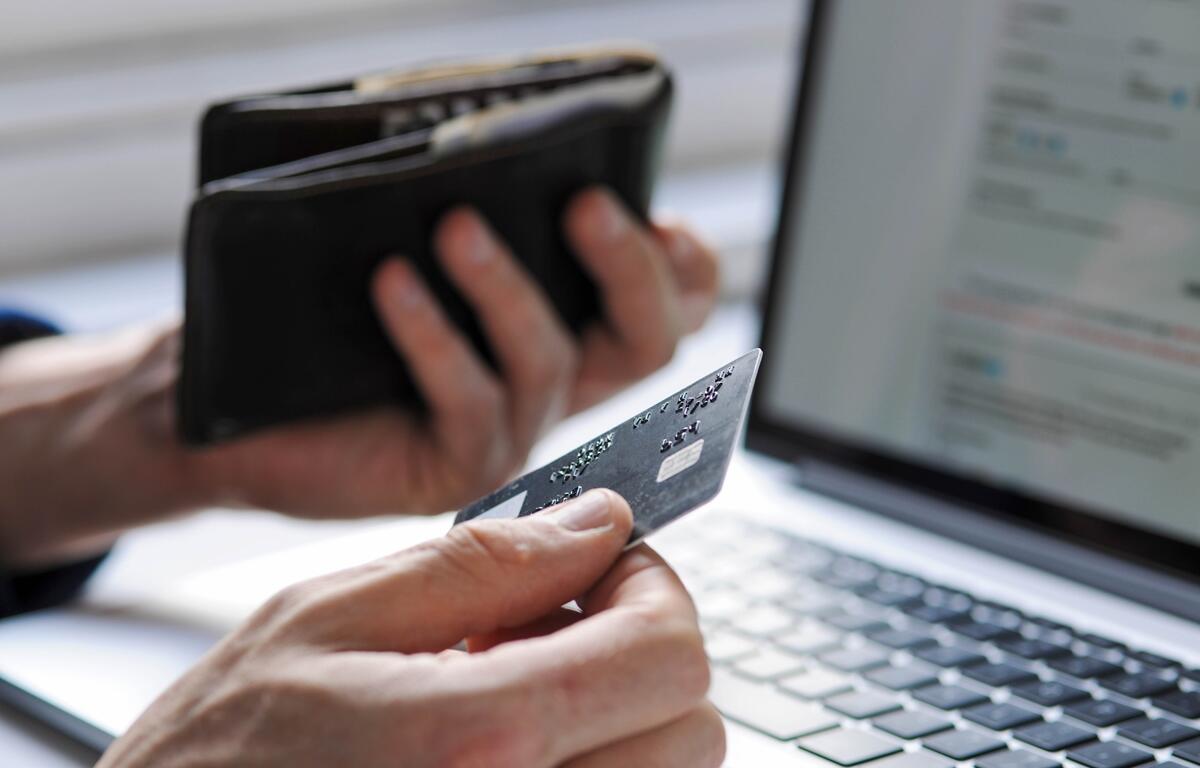 A person holds a credit card while reviewing payment information on a laptop, common scenario scammers exploit in identity theft cases.