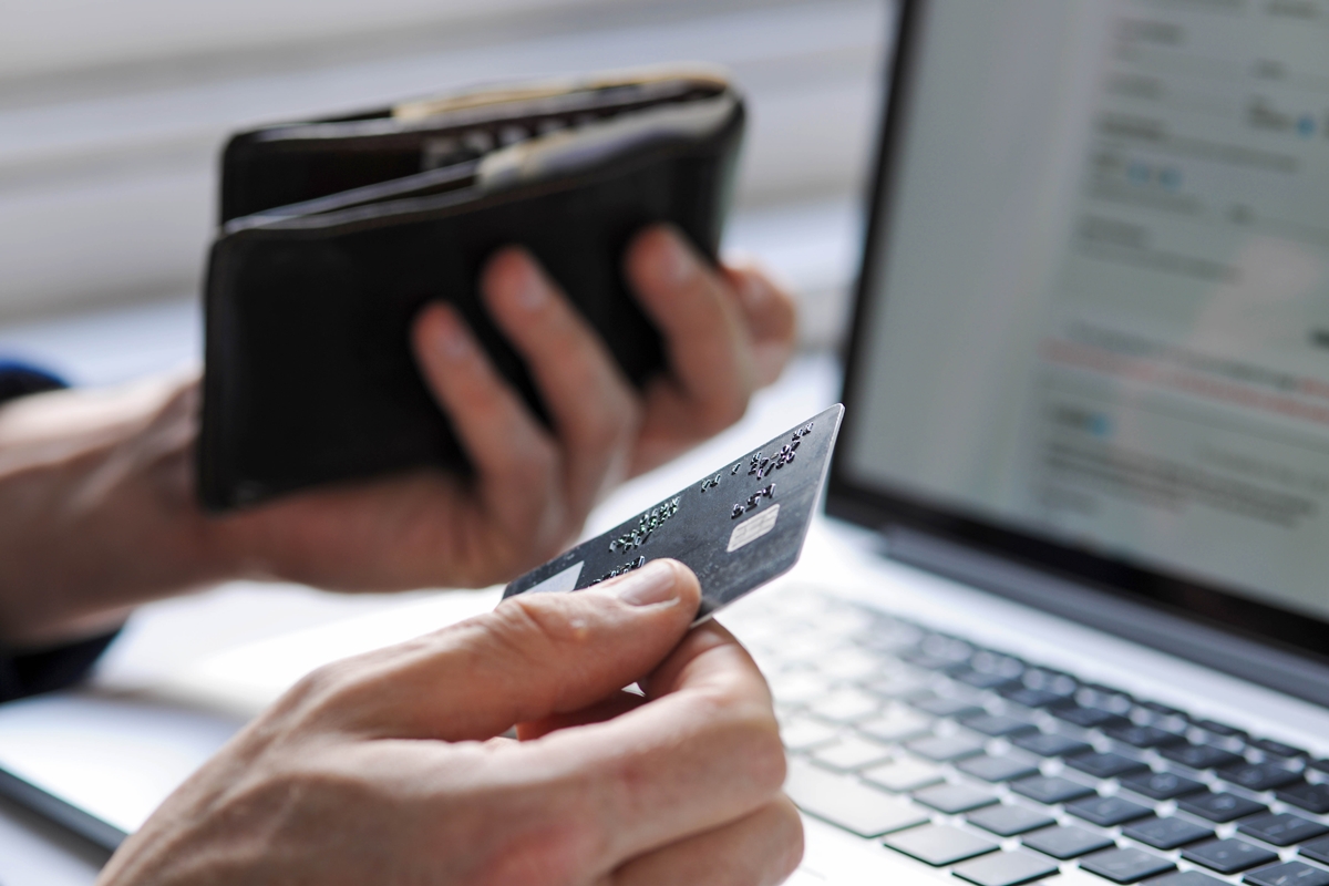 A person holds a credit card while reviewing payment information on a laptop, common scenario scammers exploit in identity theft cases.