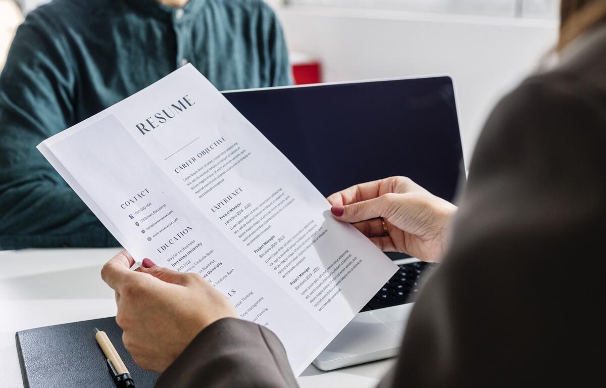 Person holding a printed resume across the table from a job candidate during an interview.