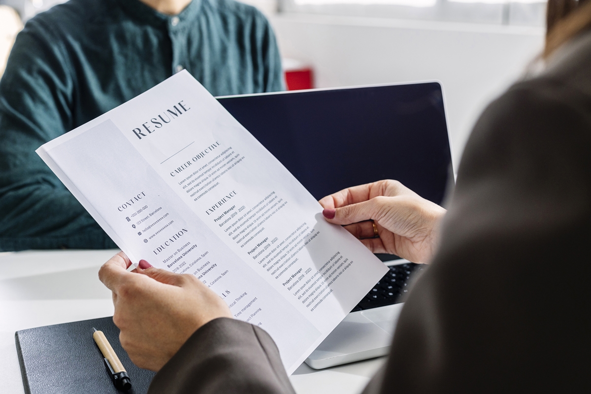 Person holding a printed resume across the table from a job candidate during an interview.