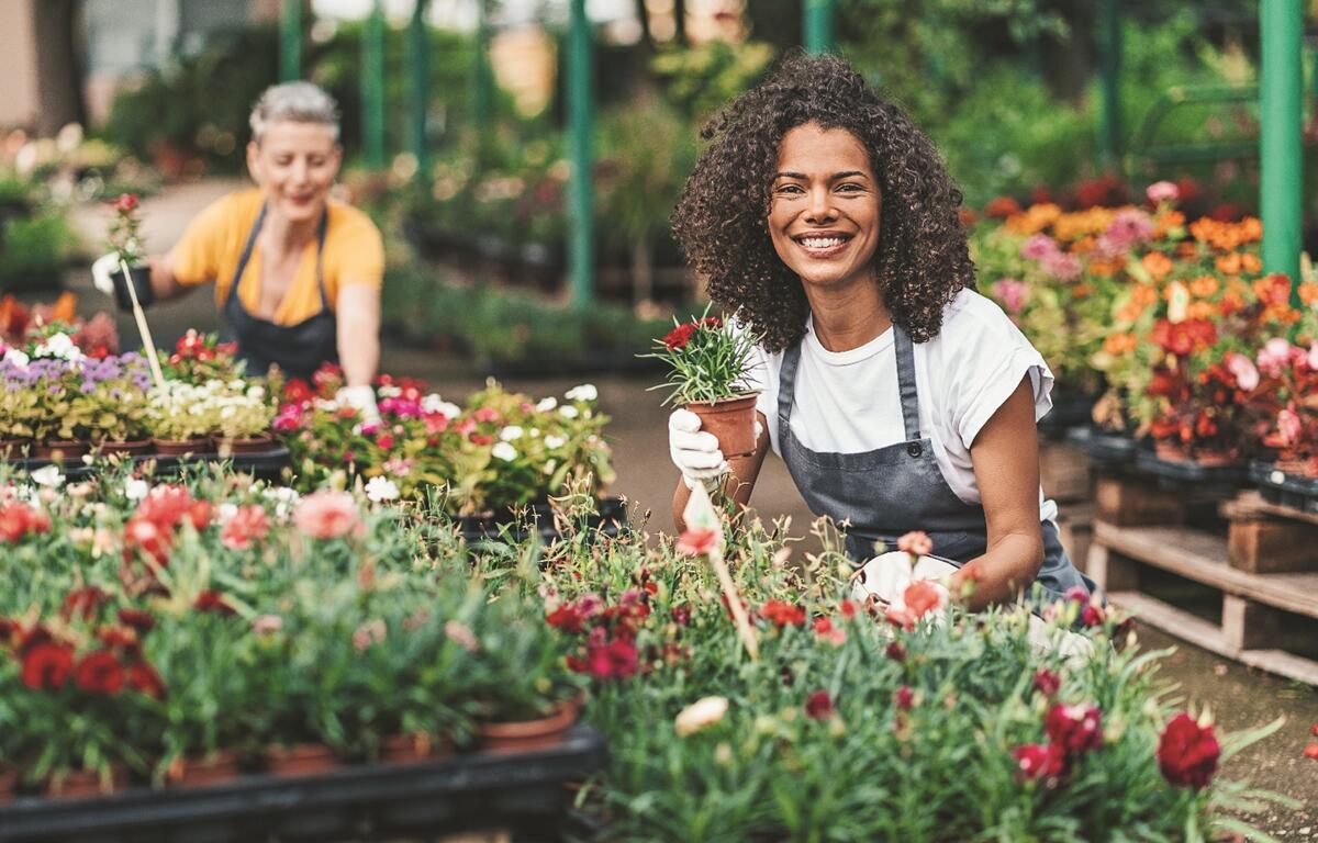 A vendor smiles while arranging plants at a flower market, one of many garden-themed displays expected at Ocala’s Big Bloom Home & Garden Show.