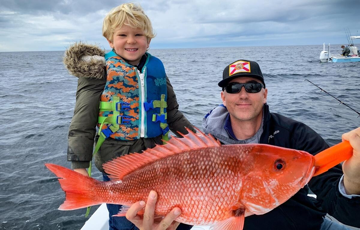 A young angler smiles with his father after catching a Gulf red snapper off the coast of Florida.