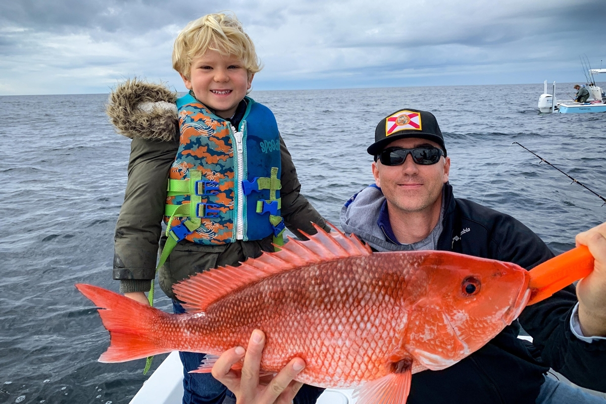 A young angler smiles with his father after catching a Gulf red snapper off the coast of Florida.