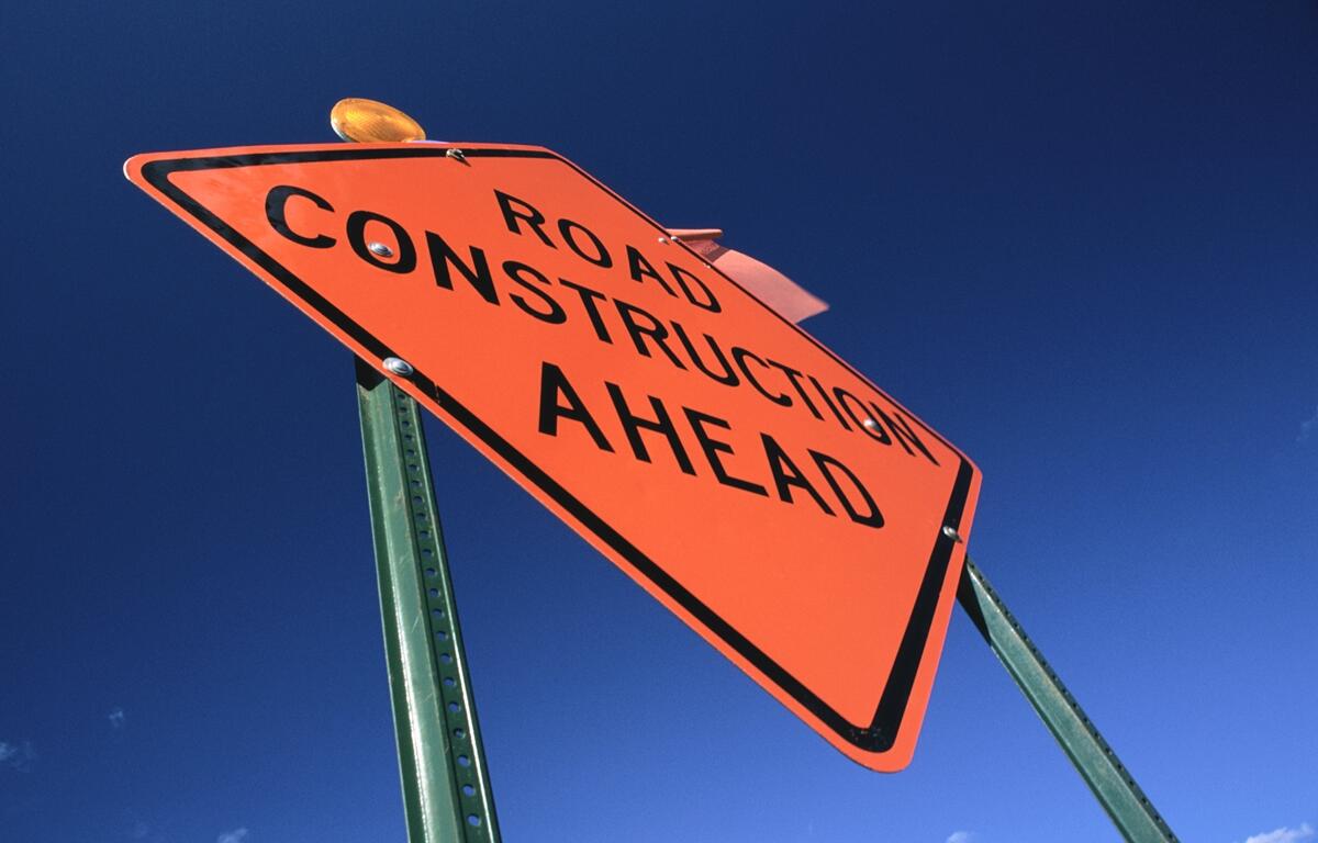 Close-up of an orange “Road Construction Ahead” warning sign against a clear blue sky.