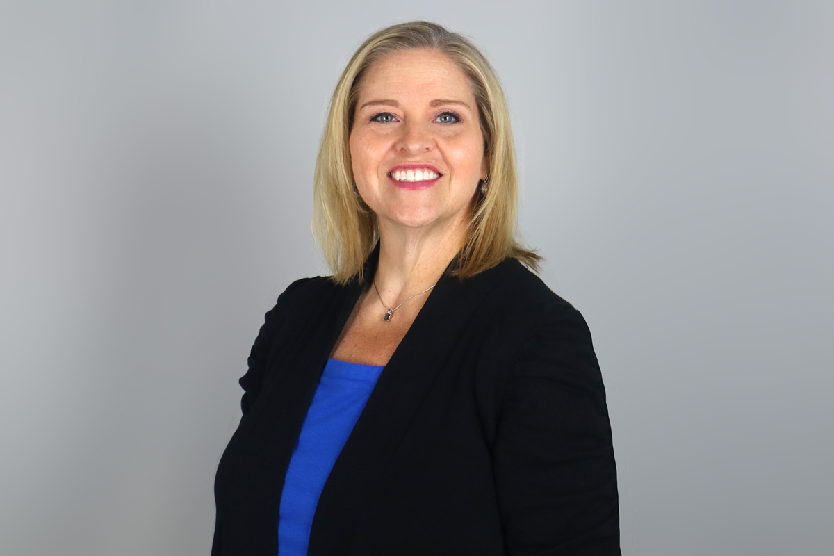 Tamara Fleischhaker, smiling in a professional headshot, wearing a black blazer and blue top against a neutral background.