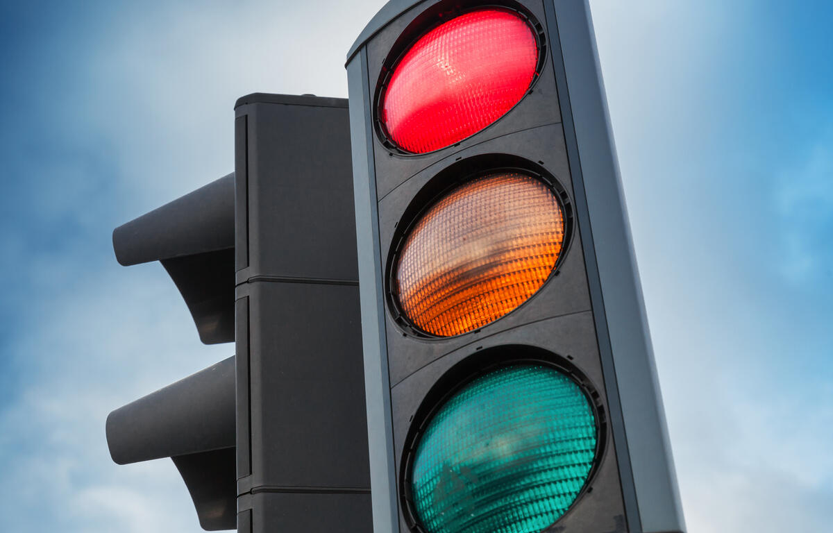Close-up of a traffic light showing red, yellow, and green signals against a blue sky.