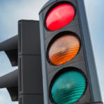 Close-up of a traffic light showing red, yellow, and green signals against a blue sky.