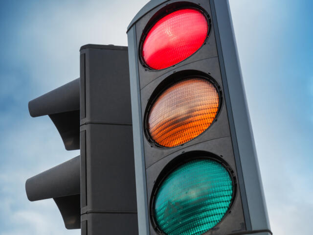 Close-up of a traffic light showing red, yellow, and green signals against a blue sky.