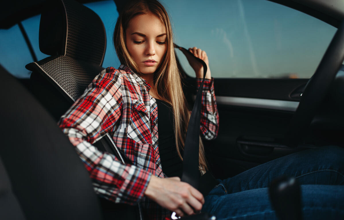 Young woman in a plaid shirt buckling her seatbelt inside a car.