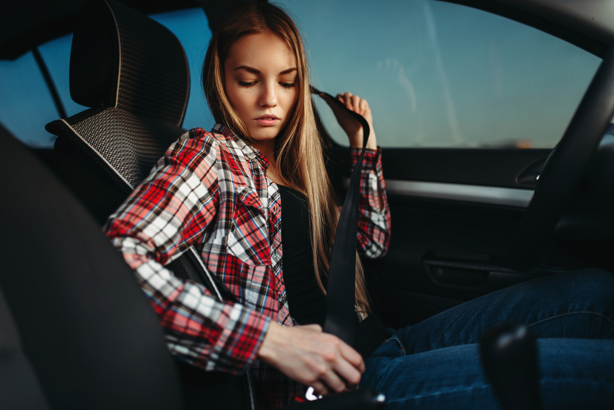 Young woman in a plaid shirt buckling her seatbelt inside a car.