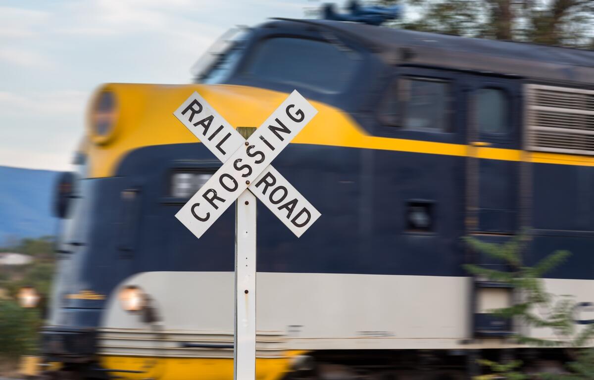 Close-up of a railroad crossing sign with a fast-moving blue and yellow locomotive blurred in the background.
