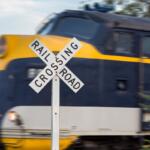 Close-up of a railroad crossing sign with a fast-moving blue and yellow locomotive blurred in the background.