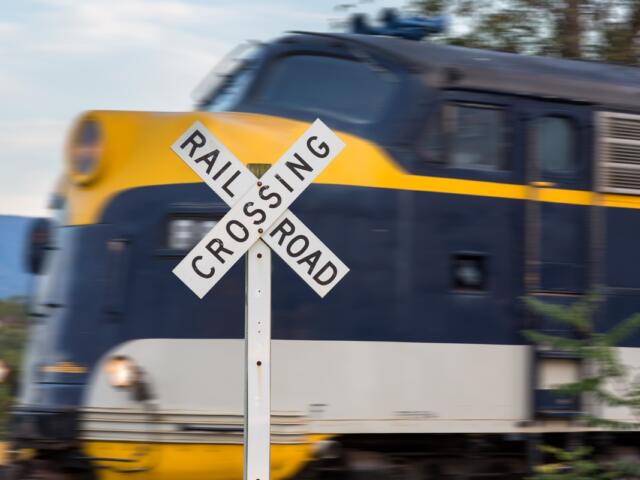 Close-up of a railroad crossing sign with a fast-moving blue and yellow locomotive blurred in the background.
