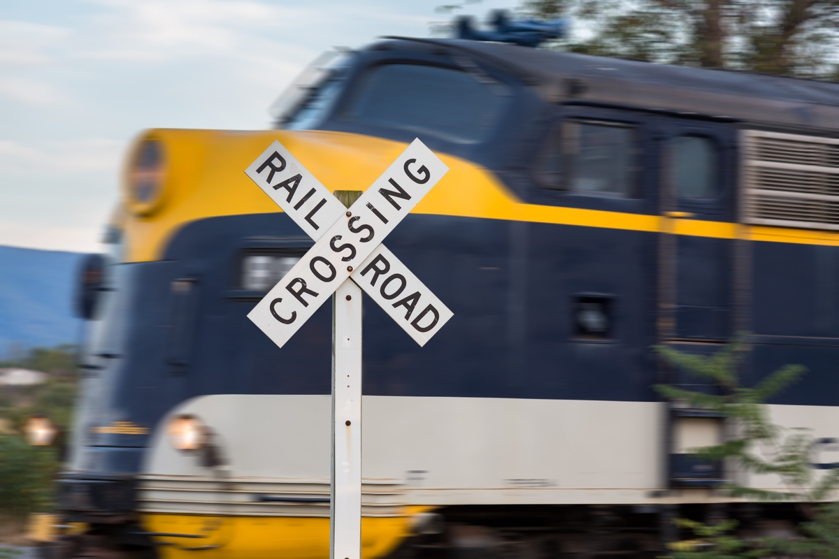 Close-up of a railroad crossing sign with a fast-moving blue and yellow locomotive blurred in the background.