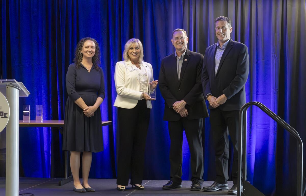 Four individuals stand on stage at the 2025 Central Florida Safety Summit as Marion County Commissioner Michelle Stone holds the Outreach Award alongside TPO Executive Director Rob Balmes. They are joined by FDOT officials Loreen Bobo and John E. Tyler in front of a blue curtain backdrop.