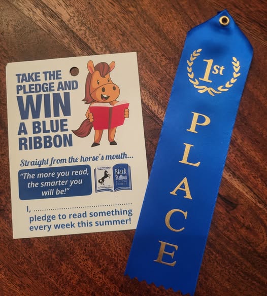 A blue “1st Place” ribbon sits next to a pledge card featuring a cartoon horse promoting summer reading with the message, “The more you read, the smarter you will be!”