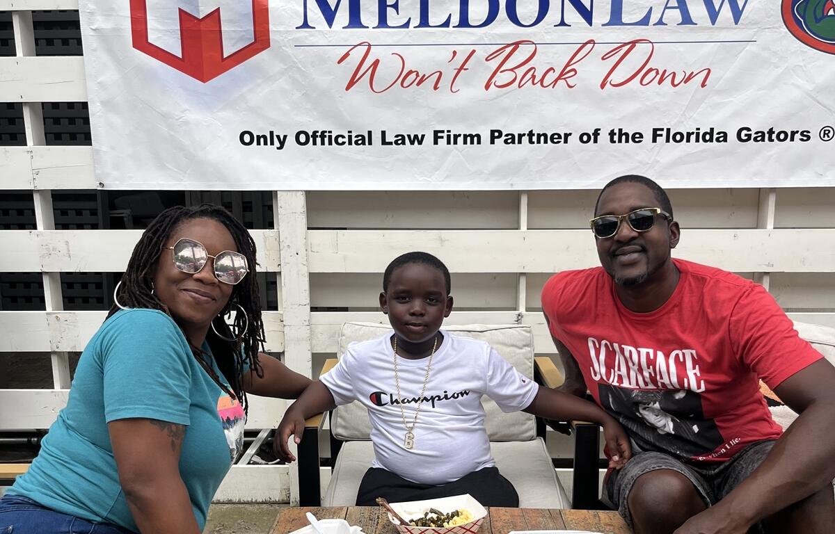 Family with child sitting at table and eating barbecue in front of sponsor banner at BBQ & Brew Festival in Williston