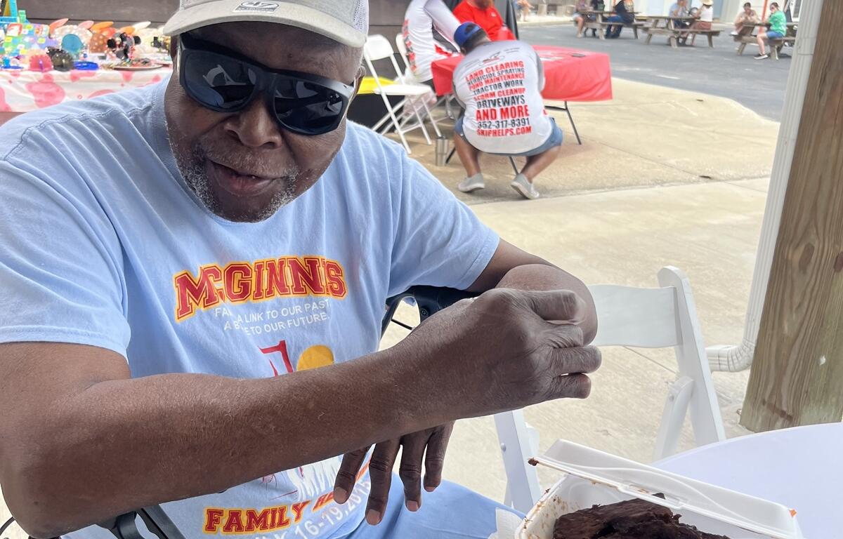 Man smiling and eating barbecue ribs at outdoor table during BBQ & Brew Festival in Williston