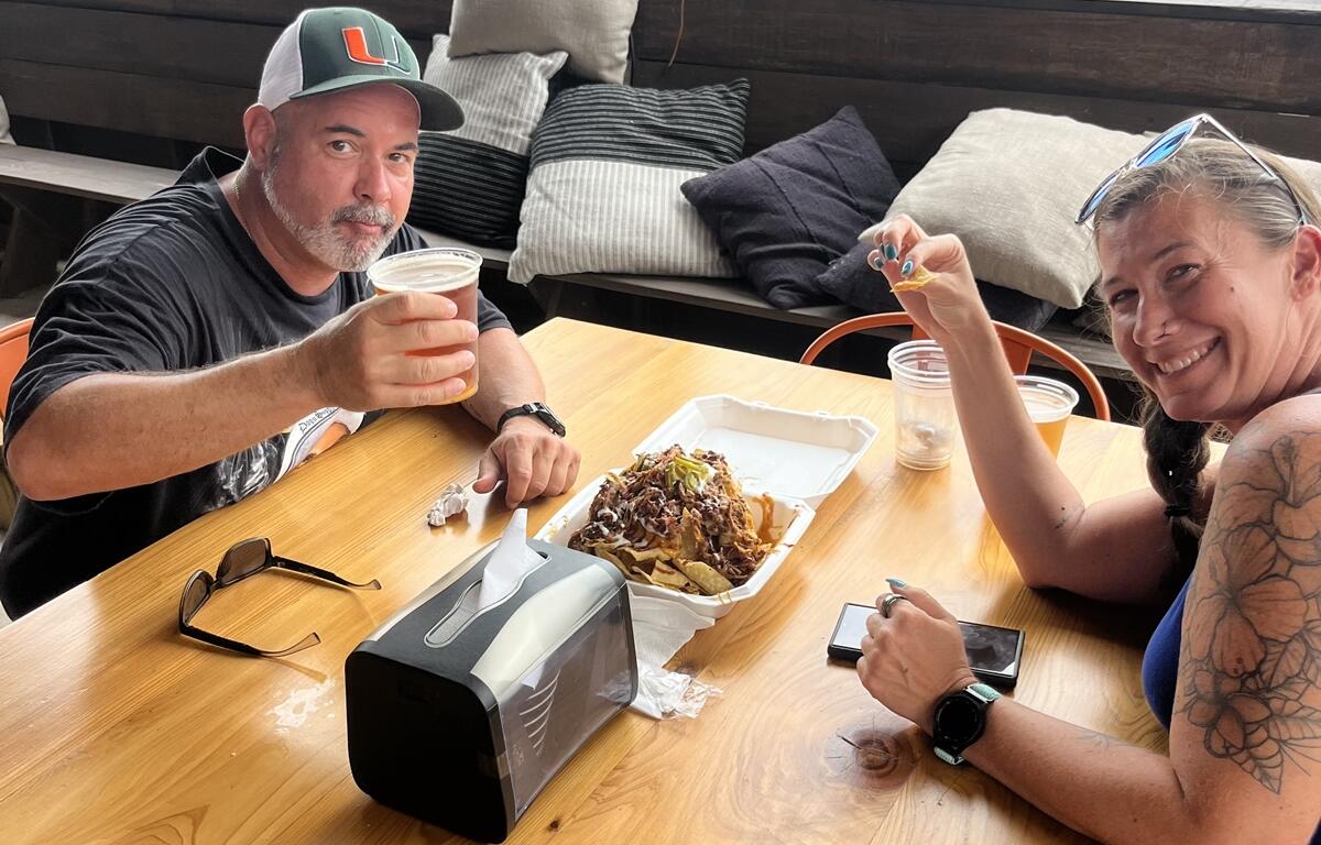 Man and woman smiling while eating barbecue nachos and drinking beer at a table during BBQ & Brew Festival in Williston